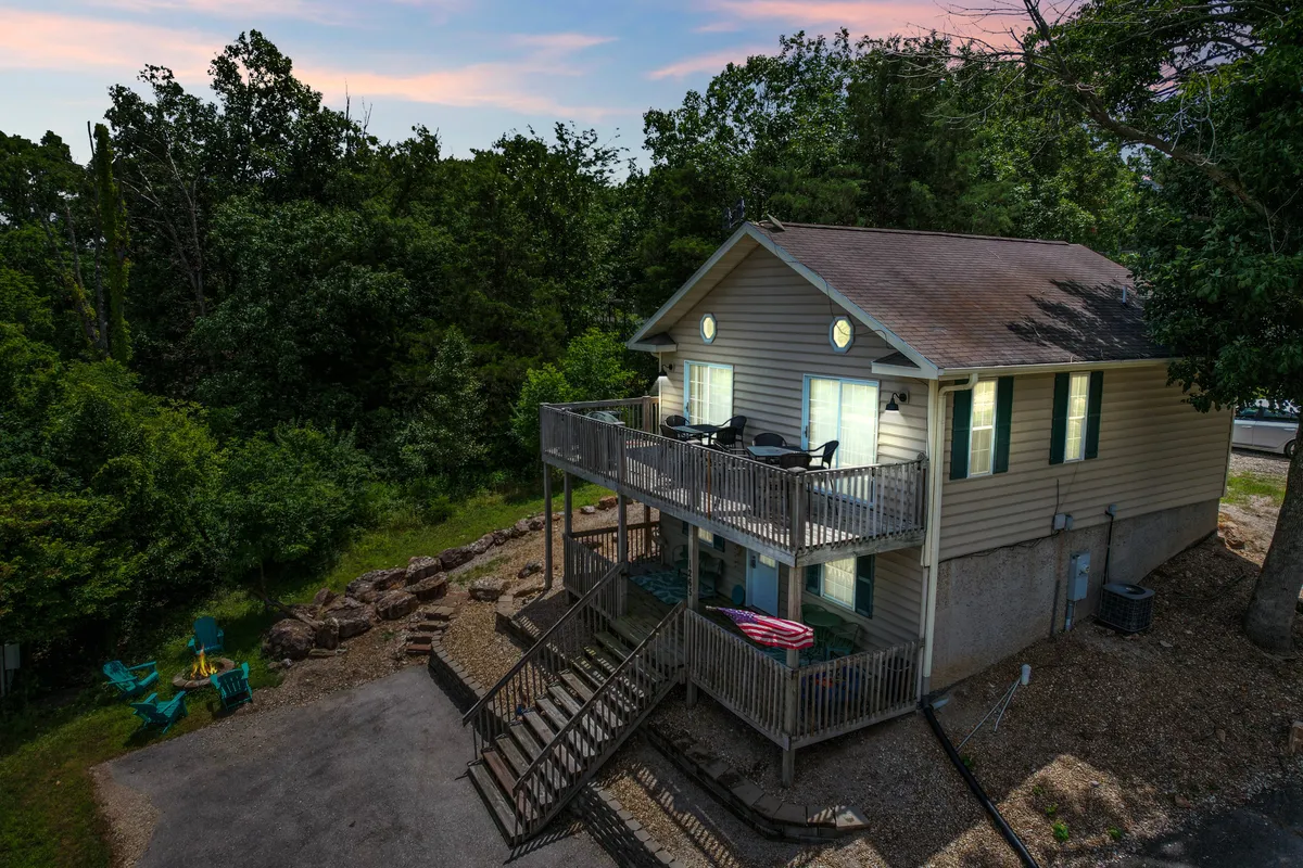 The house exterior with a well-appointed deck, chairs for gathering, a staircase leading down to landscaped grounds, and surrounding trees. The scene invites guests to imagine group activities or quiet moments. The clear view of the deck and natural setting make it instantly relatable for pet owners seeking safe outdoor spaces for their companions.