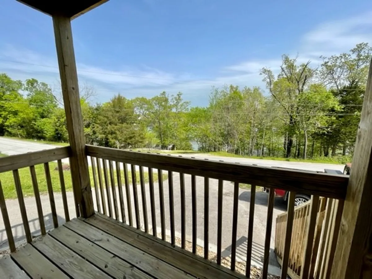 View from a wooden porch railing overlooking trees and water with a driveway below. The peaceful, open-air environment encourages exploration, sunrise watching, and wildlife observation. The presence of accessible paths and nature views makes it an ideal backdrop for leisurely walks with pets.