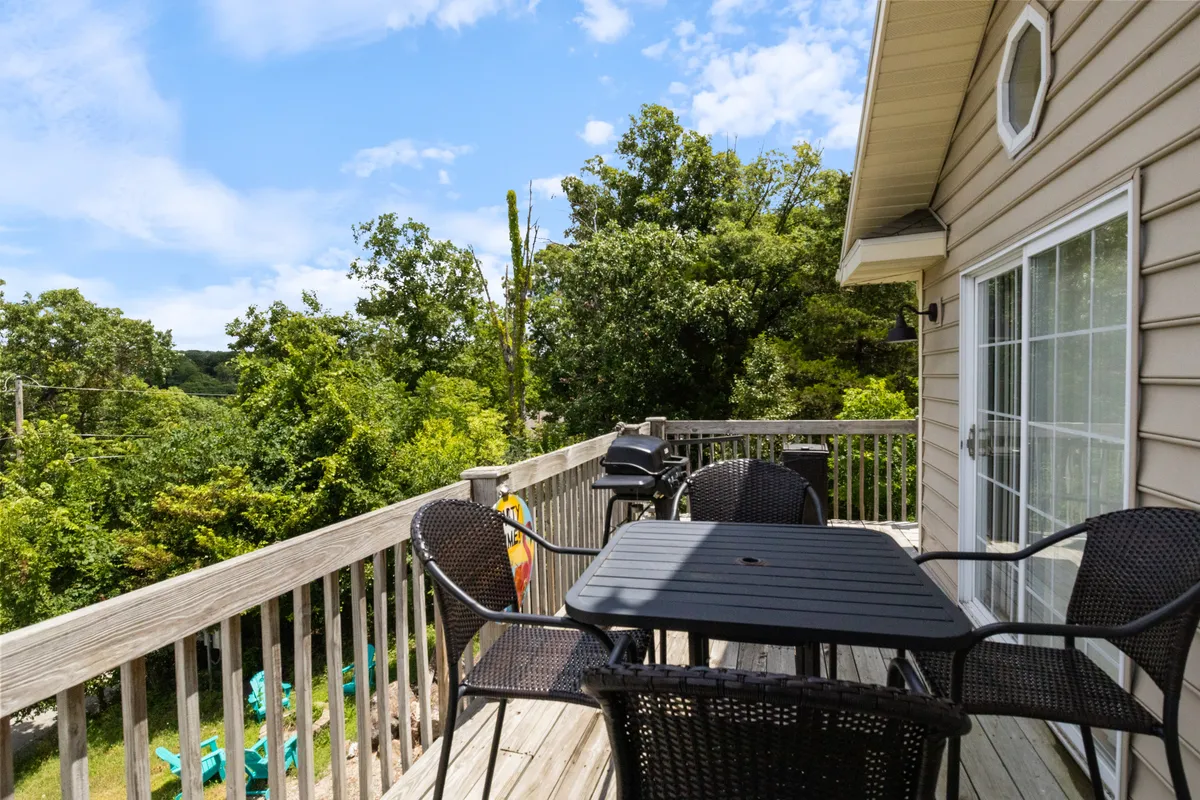 An outdoor deck furnished with comfortable seating and surrounded by lush greenery. The area includes a grill, making it ideal for group gatherings, outdoor dining, and enjoying sunset views amidst nature.