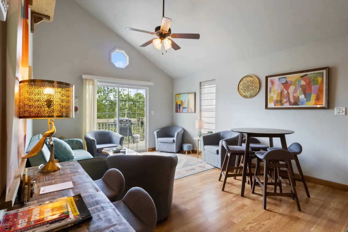 This image showcases a living room and dining area with a comfortable sofa set, a dining table, artistic wall decor, and a warm lamp. Sunlight streams through the windows, illuminating the inviting and social atmosphere ideal for gatherings.
