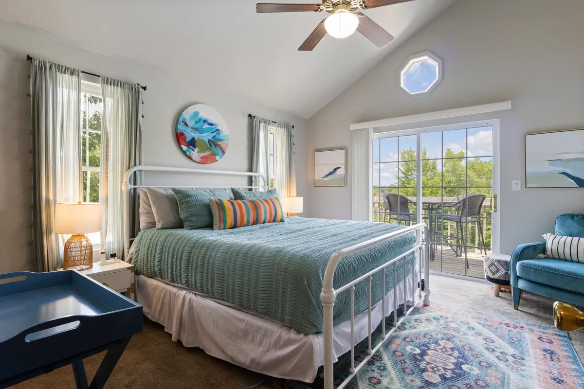 A serene bedroom featuring a plush bed with decorative pillows, a window offering a scenic view, an accent chair, and tasteful wall art. The space feels calm and cozy, ideal for unwinding after a day of activities.