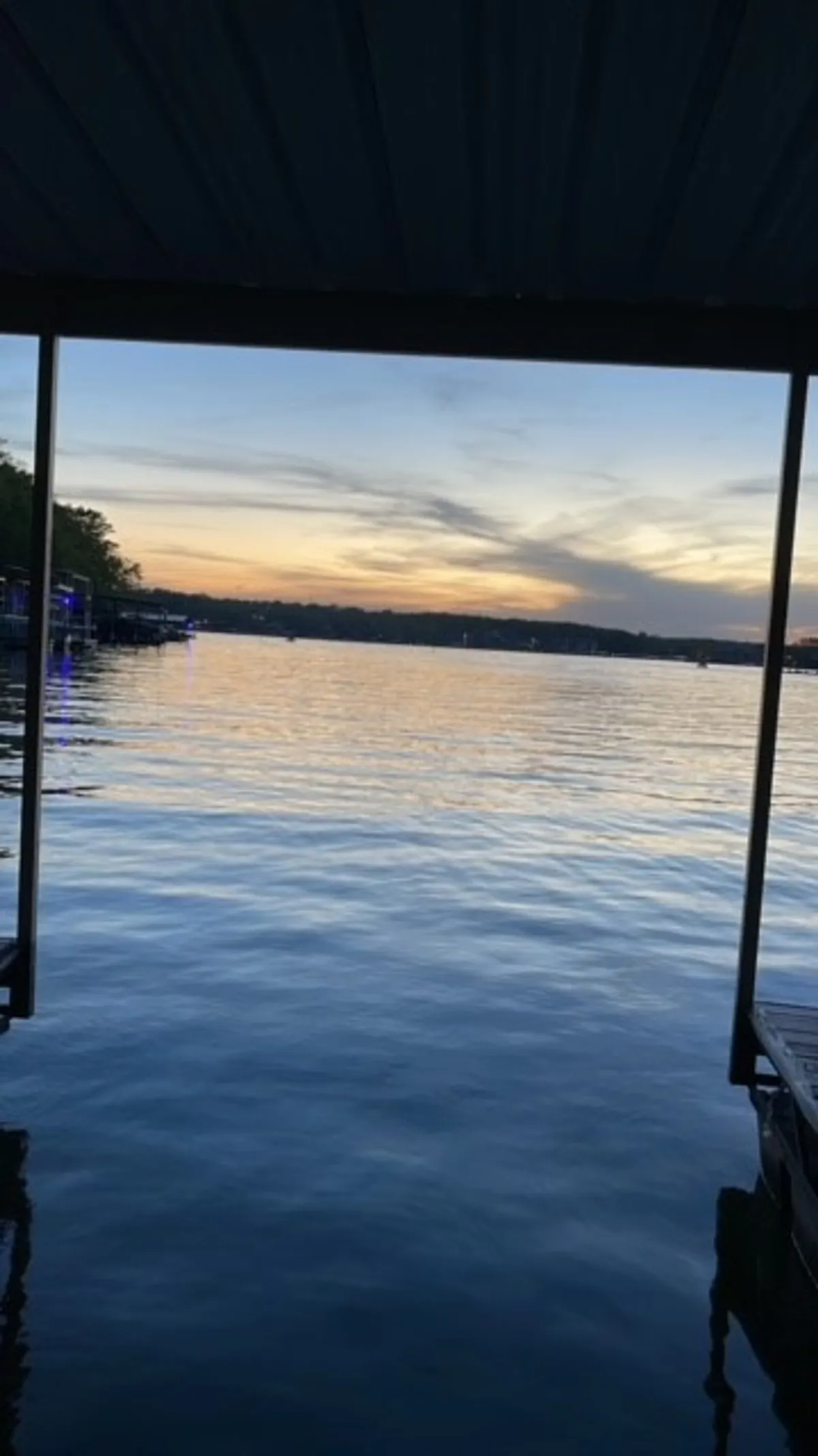 A serene sunset scene over the lake with a dock extending into calm water. The sky glows with warm colors as evening falls, creating a peaceful and idyllic backdrop. This setting suggests opportunities for fishing, swimming, and enjoying the tranquil beauty of the lake at different times of day.