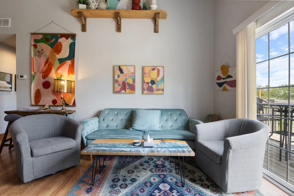 A bright, cozy living area with a plush sofa, artistic wall decor, a coffee table, and a sun-washed rug. The arrangement invites conversation or quiet moments of relaxation.