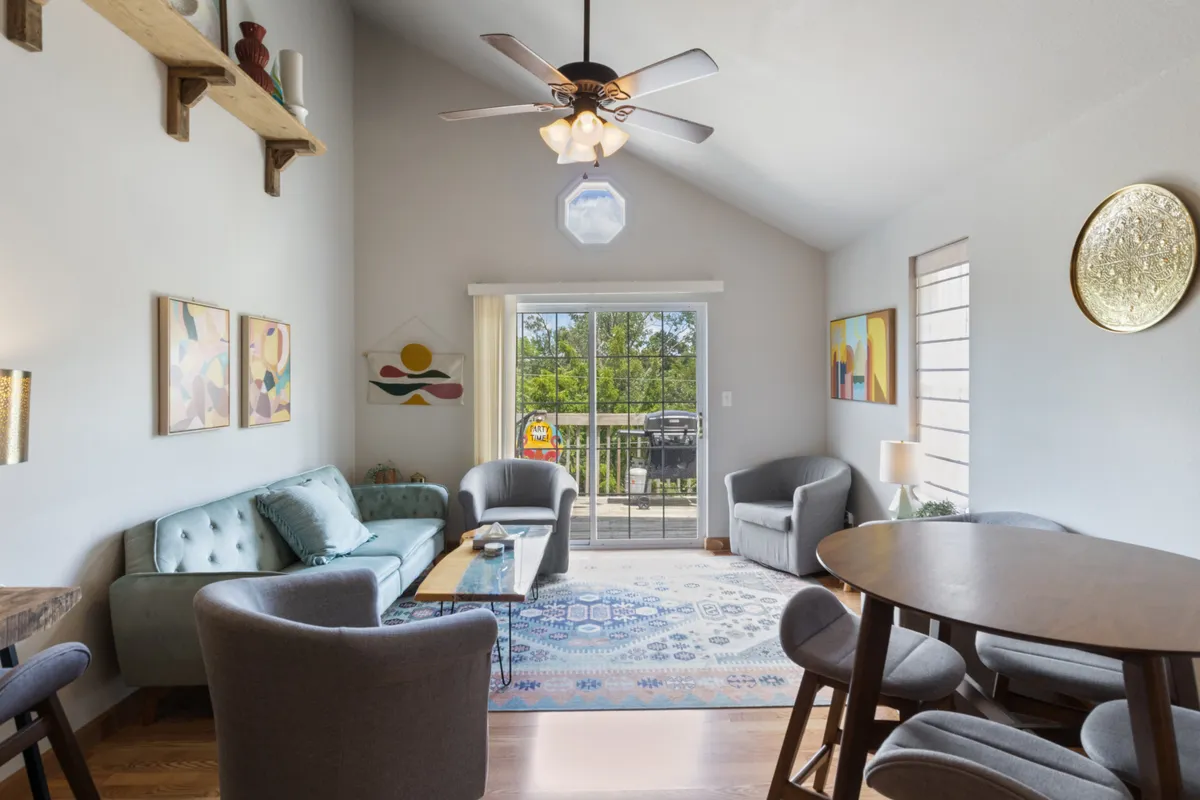 A cozy interior with a sofa, dining table, large window, and artwork. The arrangement encourages both intimate conversations and group activities, such as dining or game nights, in a light-filled, comfortable setting.