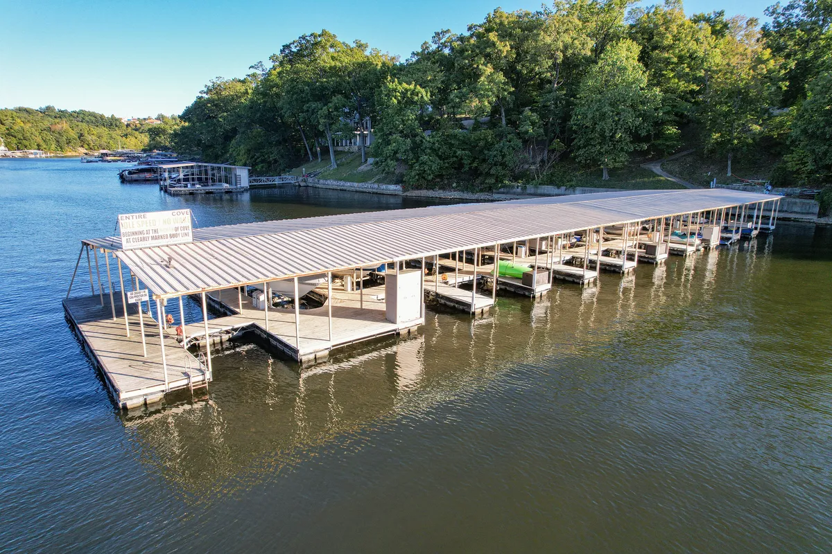 A serene dock stretches over calm lake waters, with boats tied up and a wide view of the water's surface. The setting sun casts a warm glow, inviting relaxation and the promise of adventure. The dock is clearly designed for boating, fishing, or simply soaking in the waterfront atmosphere.