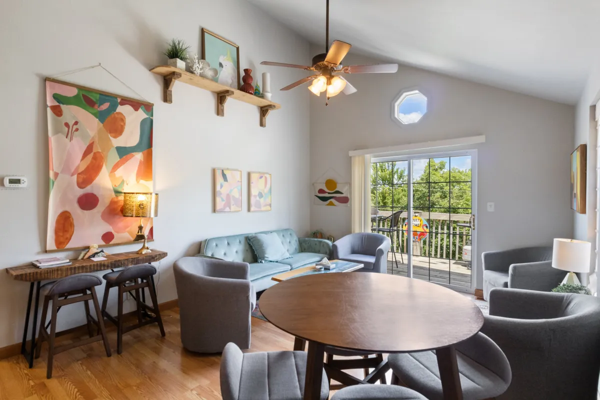 The image showcases a bright, inviting living and dining area with vibrant wall art, a plush teal sofa perfect for lounging, and a large wooden dining table ideal for group gatherings. Sunlight pours in, setting a cheerful, creative tone that invites guests to relax, chat, or share a meal together.